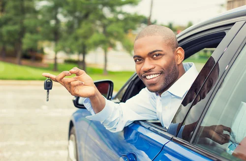 man leaning out of window of car holding keys smiling