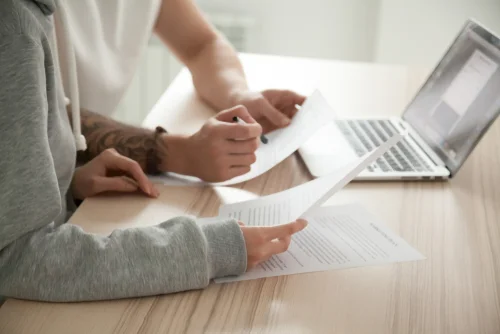 two people looking at paperwork in front of computer screen